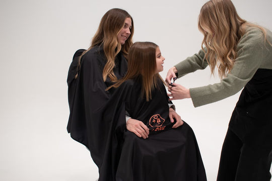 Stylist cutting child's hair while parent holds child using +ONE haircutting cape